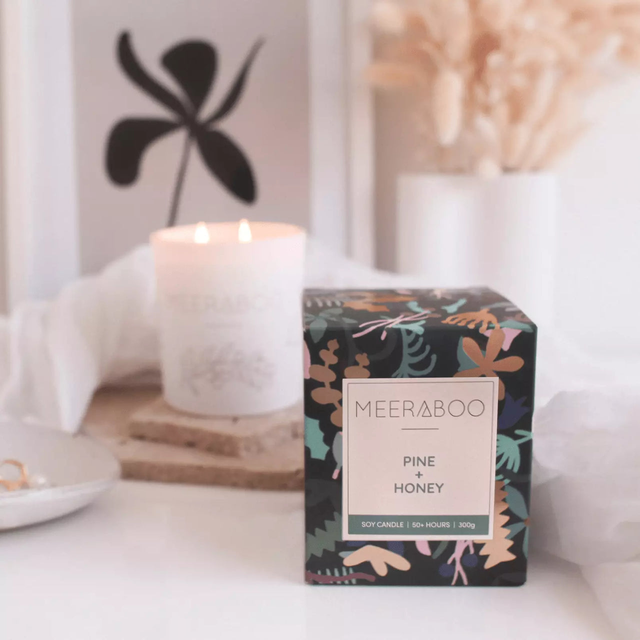 A Meeraboo Boxed Soy Candle - Pine + Honey is sitting on a table next to a candle.