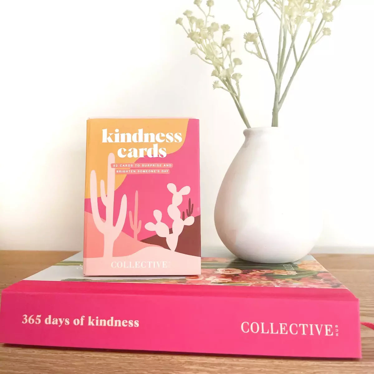 A book with Collective Hub's Kindness Cards on top of it, ready to brighten someone's day with a surprise.