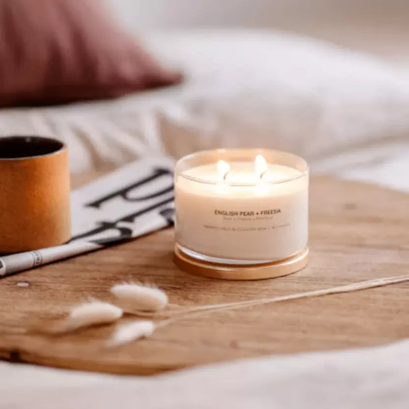 A Meeraboo Soy Candle - English Pear + Freesia sits on a wooden tray next to a newspaper.