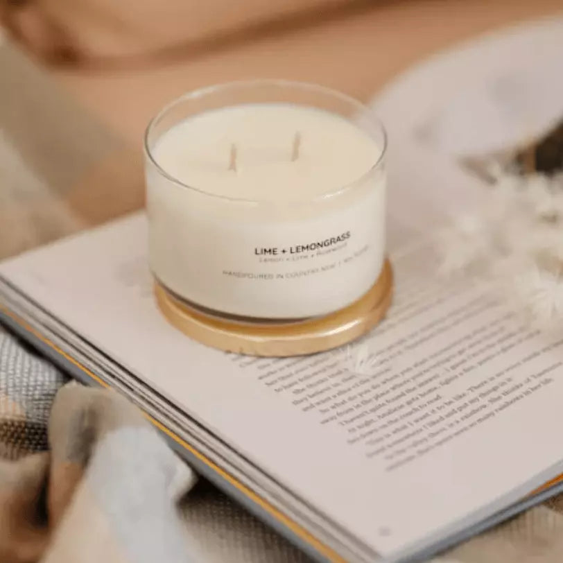 A Meeraboo Soy Candle - Lime + Lemongrass sits on top of a book on a bed.