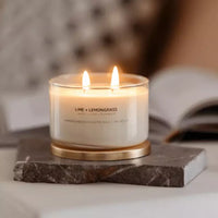 Thumbnail for A Meeraboo Soy Candle - Lime + Lemongrass sits on a marble table next to a book.