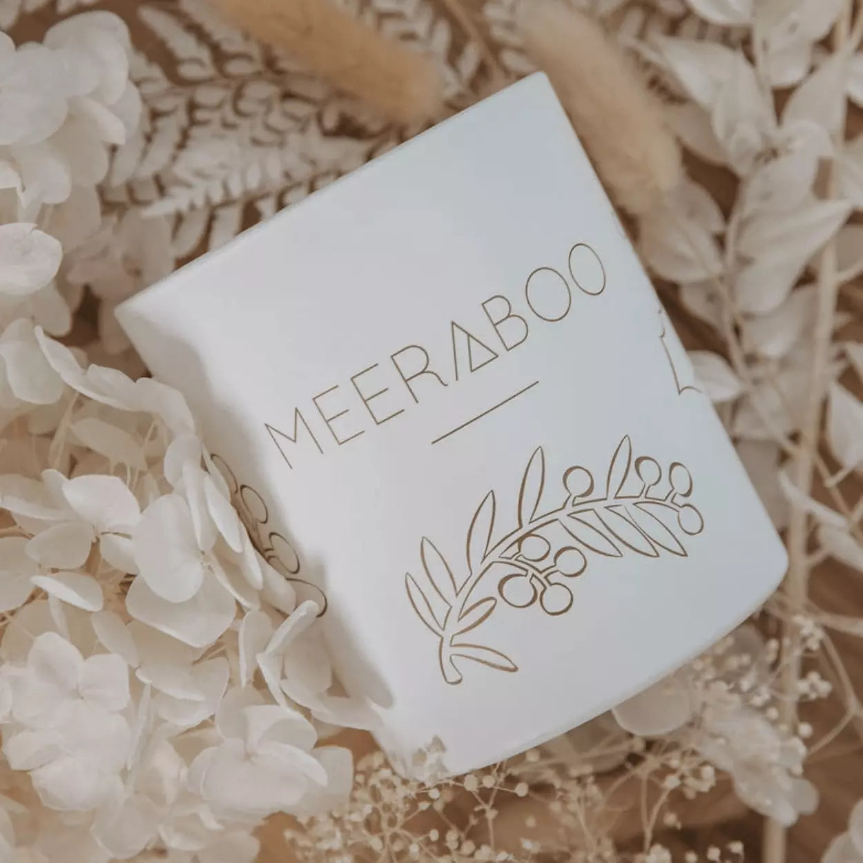A white candle with the brand name Meeraboo and the product name Boxed Soy Candle - Pine + Honey on it.