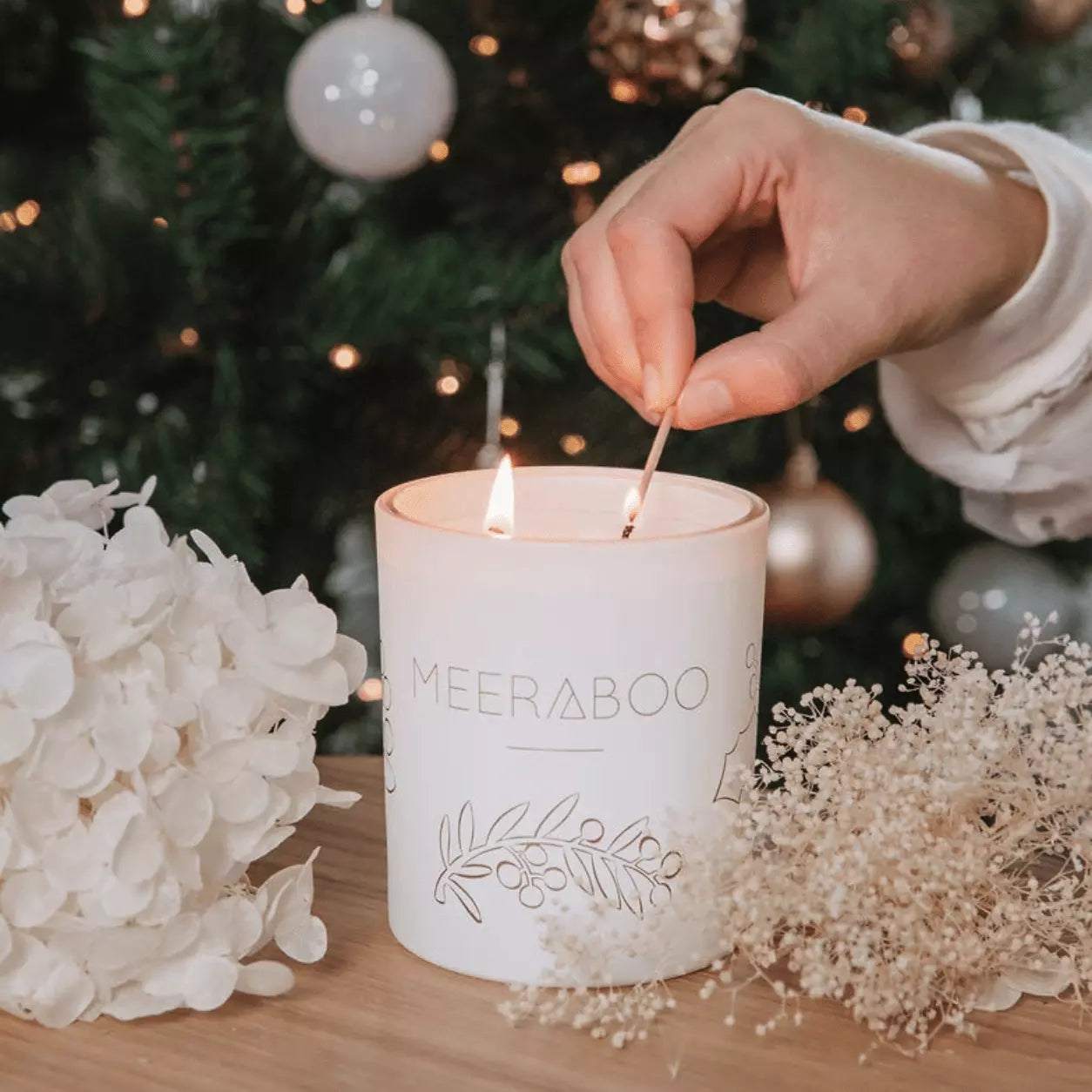 A person lighting a Meeraboo Boxed Soy Candle - Pine + Honey in front of a christmas tree.