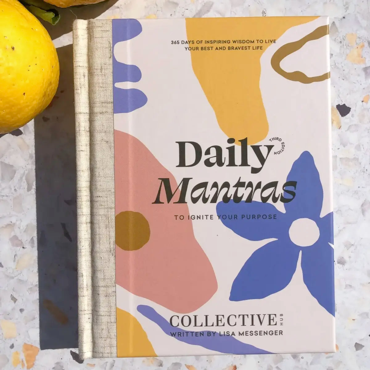 A curated book of Daily Mantras to Ignite Your Purpose - V3 with inspirational quotes next to a lemon by Collective Hub.