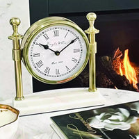 Thumbnail for A Column Clock with White Marble Base - Gold sits on a table next to a fireplace.