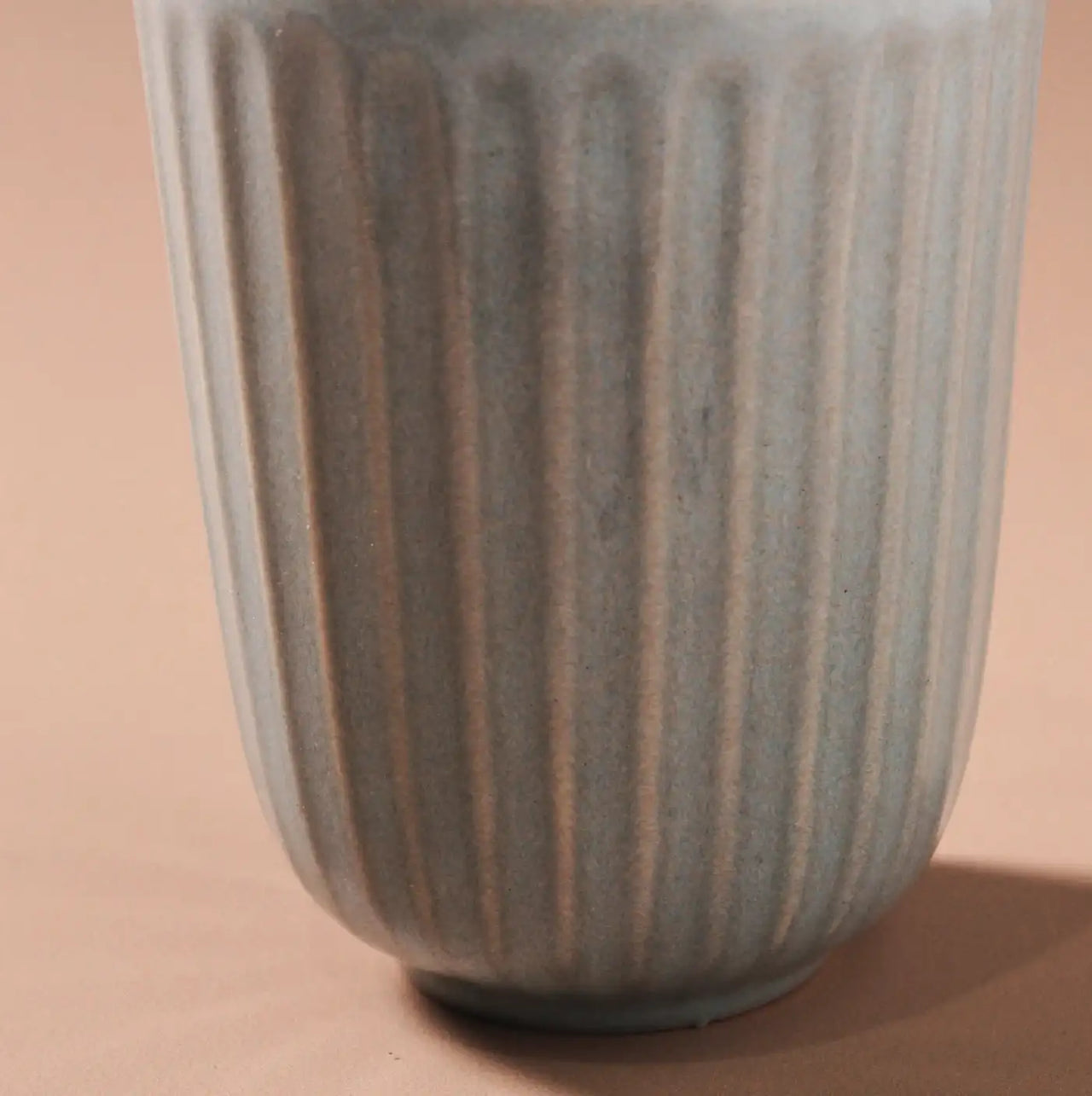 Close-up of the handcrafted Juliette Latte Mug by Indigo Love, featuring a ribbed, cylindrical design in light blue against a beige background. The vertical grooves and reactive glaze add texture and visual interest.