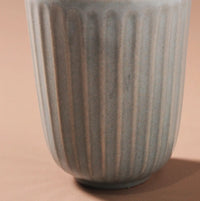 Thumbnail for Close-up of the handcrafted Juliette Latte Mug by Indigo Love, featuring a ribbed, cylindrical design in light blue against a beige background. The vertical grooves and reactive glaze add texture and visual interest.