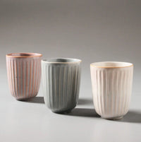 Thumbnail for The Juliette Latte Mugs by Indigo Love, featuring a reactive glaze with vertical stripes, are arranged on a light gray surface in pastel pink, gray, and white for an elegant and minimalist display.