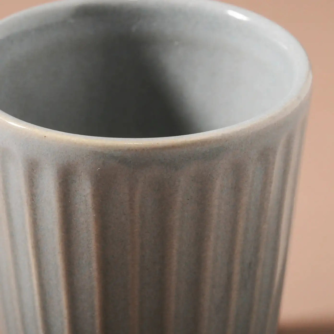 Close-up of a light gray, vertically ribbed ceramic cup on a neutral background. The handcrafted Juliette Latte Mug - Light Blue by Indigo Love showcases a smooth surface with subtle reactive glaze variations in shade, enhancing its minimalist and elegant appearance.