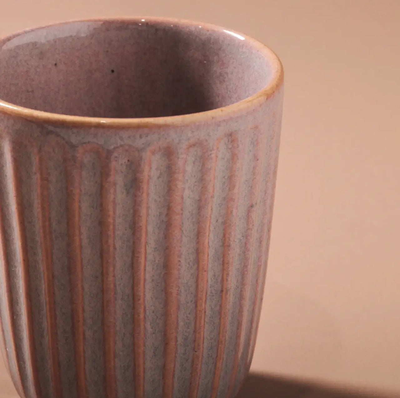 Close-up of Indigo Loves Juliette Latte Mug in Pink, showcasing its textured ribbed design. The lighting emphasizes its matte finish and delicate tonal variations, enhanced by a reactive glaze. The backdrop is softened with a neutral tone.