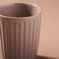 Thumbnail for Close-up of Indigo Loves Juliette Latte Mug in Pink, showcasing its textured ribbed design. The lighting emphasizes its matte finish and delicate tonal variations, enhanced by a reactive glaze. The backdrop is softened with a neutral tone.