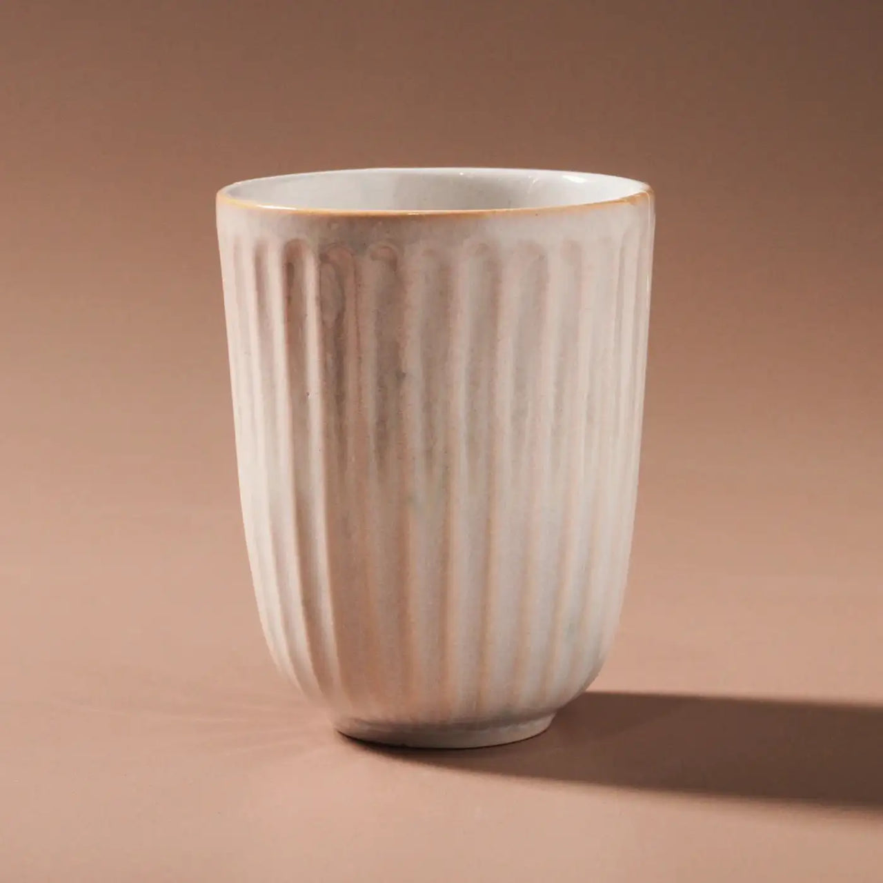 The Juliette Latte Mug - White by Indigo Love features a vertical ribbed texture on brown, a hand-finished ceramic design with an off-white sheen, subtle tapering, and a reactive glaze effect.