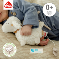 Thumbnail for A baby in blue pajamas cuddles the Pilbeam FehnNATUR Mini Musical Sheep, featuring the Fehn logo, a 0+ months label, and icons for organic cotton and a musical box that plays Brahms lullaby.