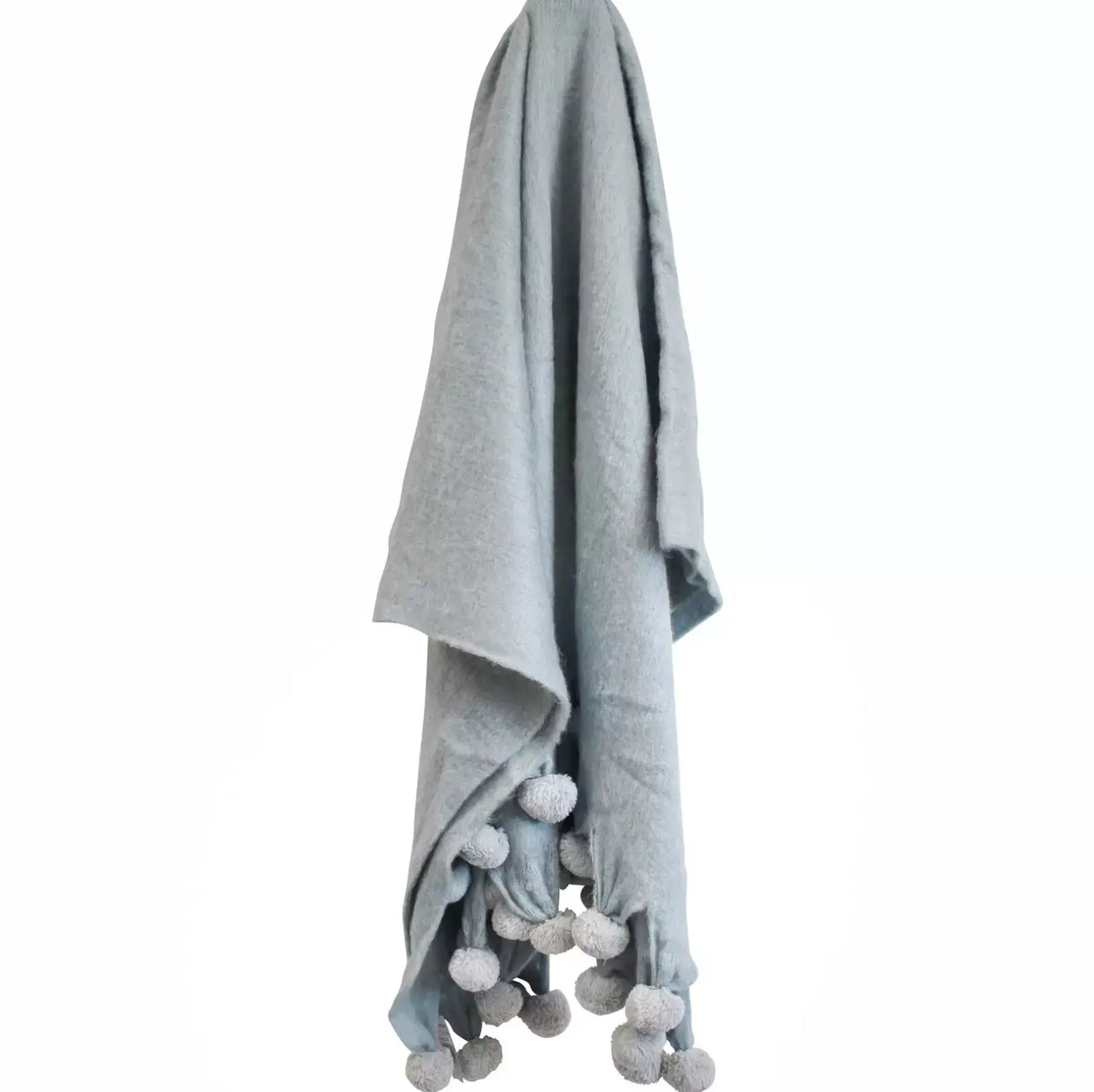 A LaVida Prussian Throw Rug with grey pom poms hanging on a hanger.