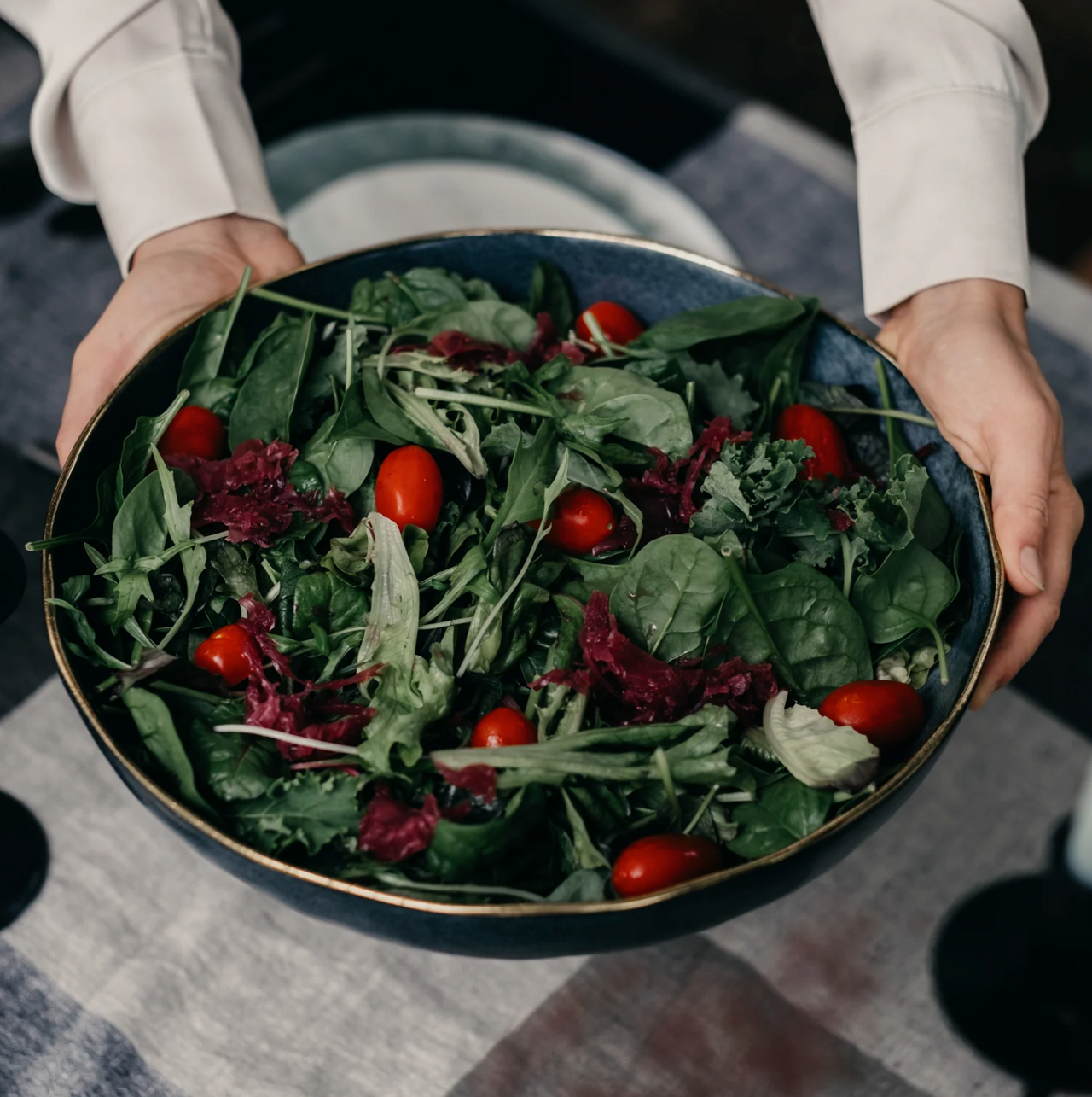 A person holding an Indigo Love Ariel Salad Bowl - Matt Black filled with greens and tomatoes.