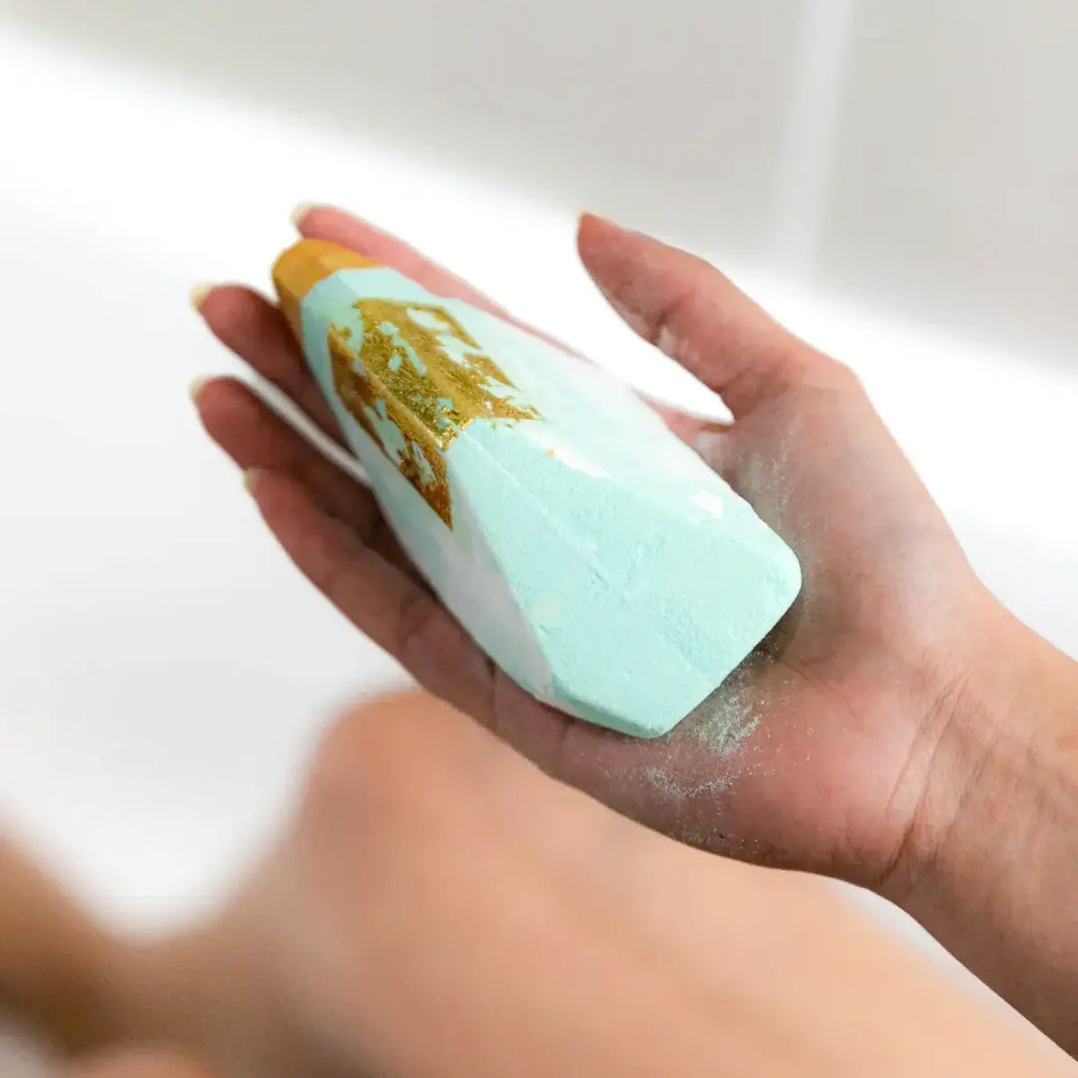 A person indulging in aromatherapy while holding a Summer Salt Body Crystal Bath Bomb - Aquamarine - Lemongrass in a bathtub.