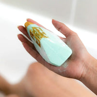 Thumbnail for A person indulging in aromatherapy while holding a Summer Salt Body Crystal Bath Bomb - Aquamarine - Lemongrass in a bathtub.
