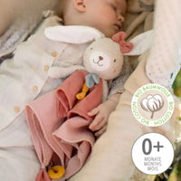 Thumbnail for A baby cuddles the FehnNATUR Comforter Hare by Pilbeam, a soft white plush toy with pink dress and bow. The BIO COTTON badge shows it’s organic cotton, and the 0+ months label supports gentle sensory development.