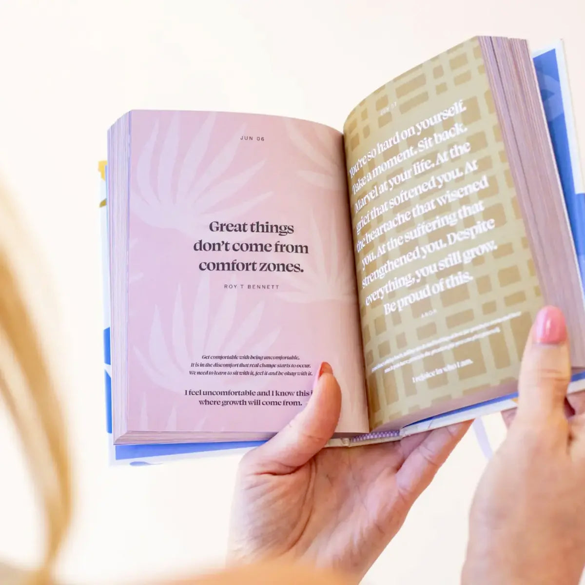 A woman holding an open book with "Daily Mantras to Ignite Your Purpose - V3" by Collective Hub for inspiration.