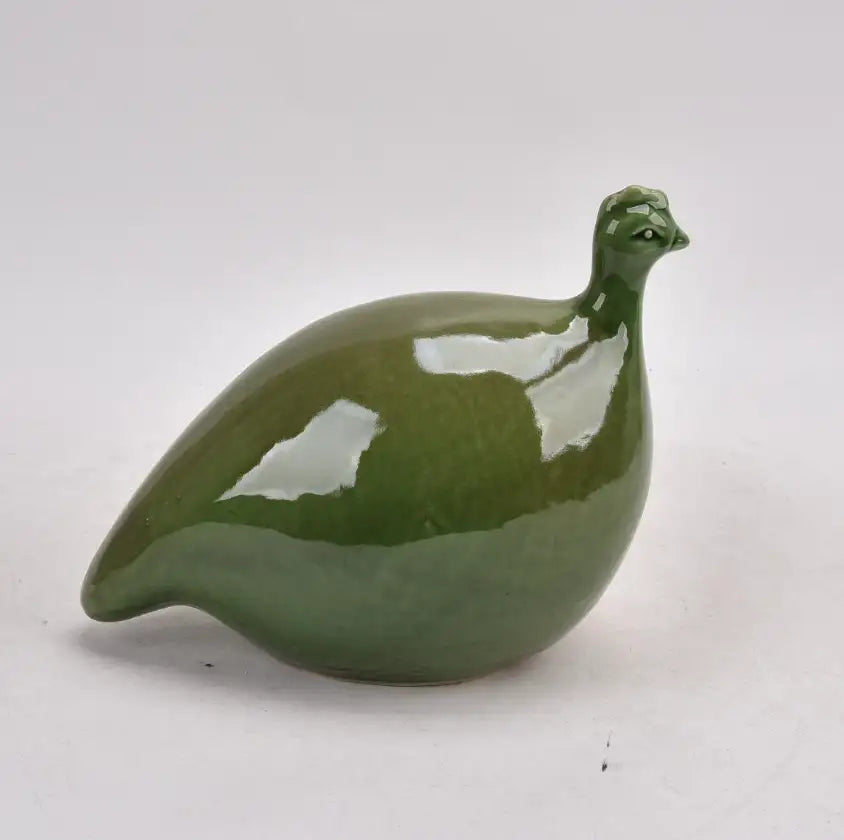 The Mode Guinea Fowl by Mediterranean Markets is a glossy green handcrafted ceramic bird sculpture with a rounded body and small head, adding an elegant decorative accent to any light gray surface.