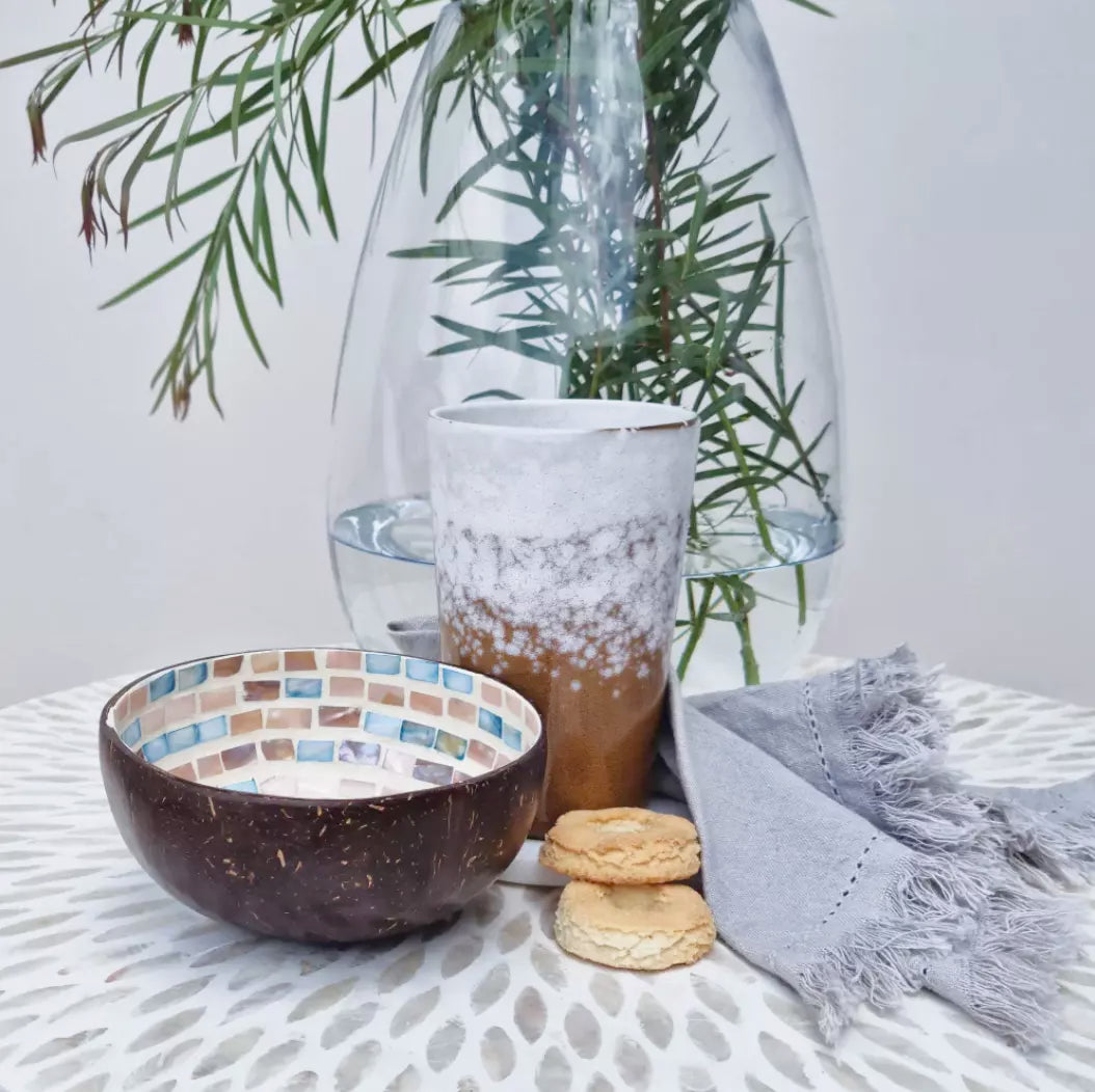 A beautiful Nacre Dashed Coconut bowl filled with delicious cookies and accompanied by a steaming cup of coffee sits on the table.