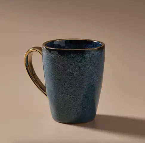 An Indigo Love Senseo Mug - Deep Blue with a gold handle on a beige background.
