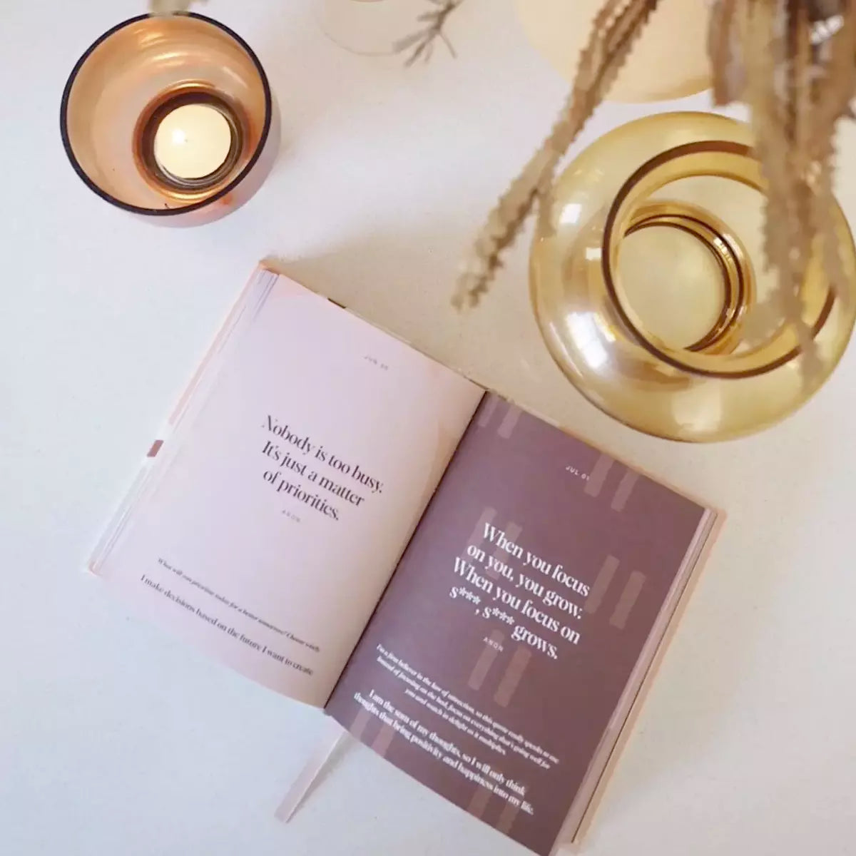 A book of Daily Mantras to Ignite Your Purpose Second Edition by Collective Hub is open on a table next to a candle.