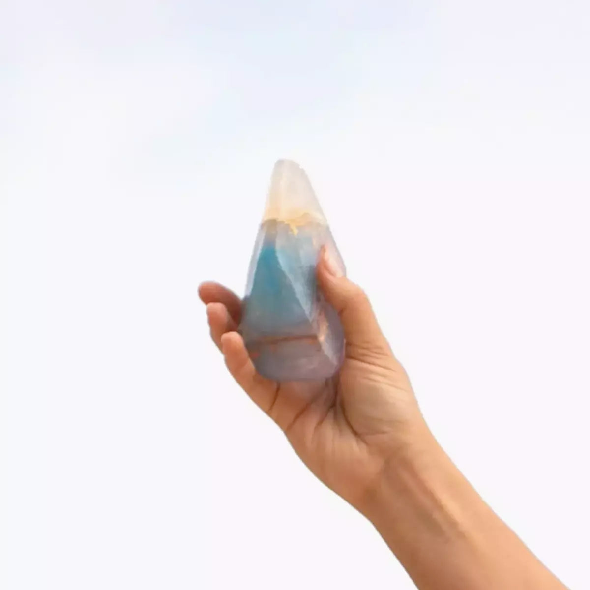 A person's hand holding a Crystal Soap - OPAL - Coconut + Vanilla Quartz Point used for skincare purposes by Summer Salt Body.