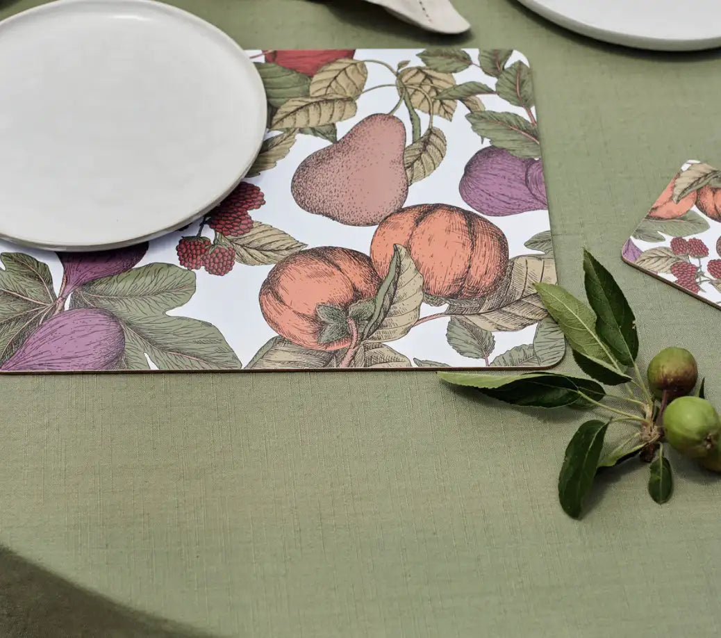 A table set with rustic charm features a green tablecloth, a white plate on the Madras Link Placemat Orchard Rectangle - S/4 with hand-painted fruit prints, and a small branch of green apples on the side.
