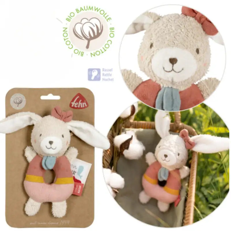 The FehnNATUR Soft Ring Rattle Hare by Pilbeam is an organic cotton baby toy with long white ears, a pink bow, blue scarf, and a pink-yellow ring-shaped body—perfect for supporting motor skill development. Shown up close and in a basket with cotton plants.