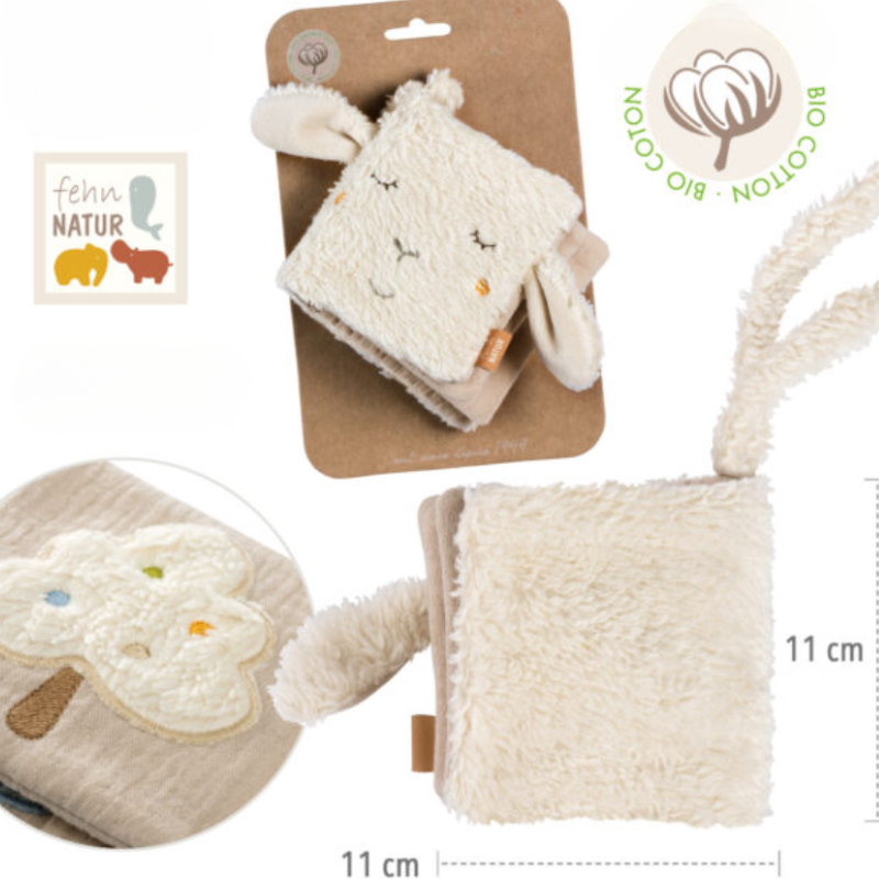 The Pilbeam FehnNATTUR Soft Book Sheep is a plush, cream-colored sensory activity toy shaped like a sheep with floppy ears and embroidered details. Made from organic cotton, it measures 11x11 cm and features an embroidered tree and eco-friendly Bio Cotton label.