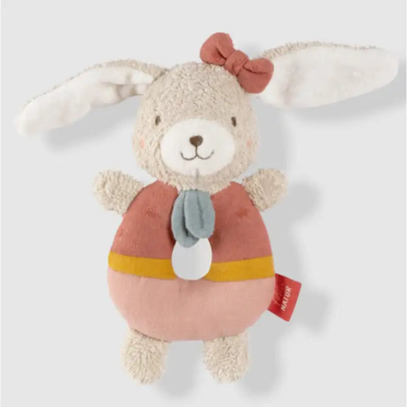The Pilbeam FehnNATUR Soft Ring Rattle Hare is a plush motor skills toy made from organic cotton with floppy white ears, pink bow, smiling face, pink body with yellow stripe and blue scarf, plus a red tag for extra baby development fun.